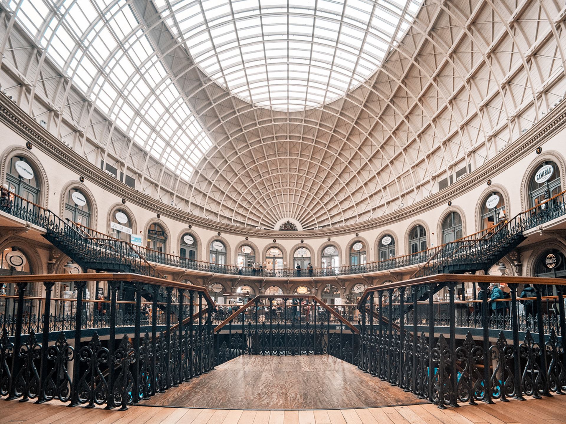 Interior of a historic covered arcade with glass dome ceiling and curved balconies.
